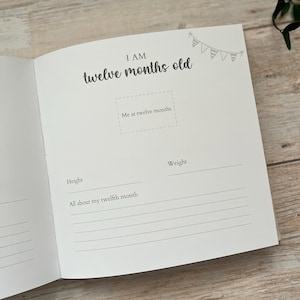 May include: Open baby memory book page with the text "I AM twelve months old." The page includes prompts for height, weight, and a space for a photo. A small banner illustration is in the upper right corner.