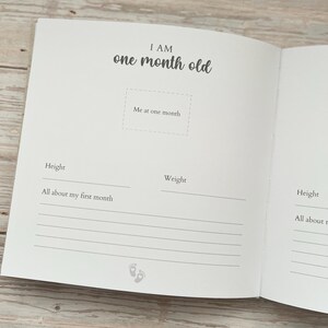 May include: Open baby memory book with the text "I AM one month old." The book has space to record height, weight, and other details. Includes a section for a photo and a line for "All about my first month."