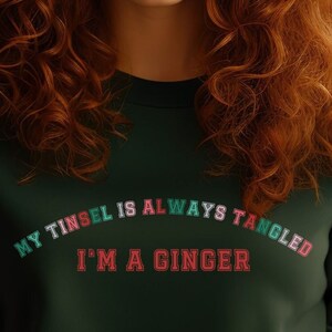 May include: Dark green sweatshirt with the text "MY TINSEL IS ALWAYS TANGLED I'M A GINGER" in white, green, and red lettering. The sweatshirt is a crew neck style.