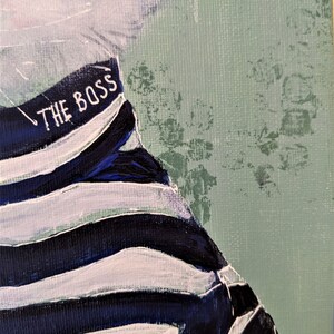 May include: A close-up of a painting of a person wearing a striped shirt with the text "THE BOSS" on it. The background is a light green color.