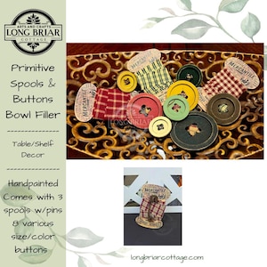 May include: A collection of sewing notions including three spools wrapped in plaid fabric with pins and eight assorted buttons in red, yellow, green, and dark brown. The items are displayed in a decorative gold-toned bowl with an ornate cutout pattern.