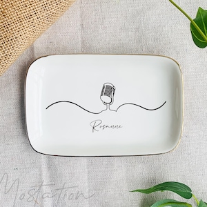 Könnte beinhalten: Weiße Keramik-Schmuckschale mit goldenem Rand. Die Schale zeigt eine schwarze Linienzeichnung eines Mikrofons mit dem Namen "Rosanne" darunter.