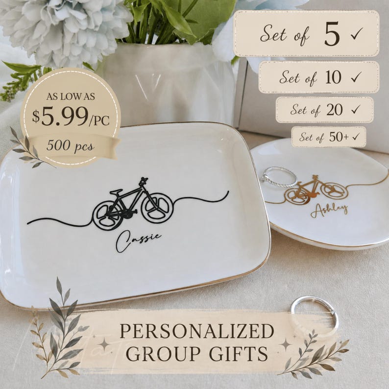 May include: Two white ceramic trinket dishes with gold-toned rims. The rectangular dish features a black line-art bicycle graphic and the name Cassie. The round dish features a gold line-art bicycle graphic and the name Ashley. Text includes Set of 5, 10, 20, 50+, AS LOW AS $5.99/PC 500 pcs, and PERSONALIZED GROUP GIFTS.