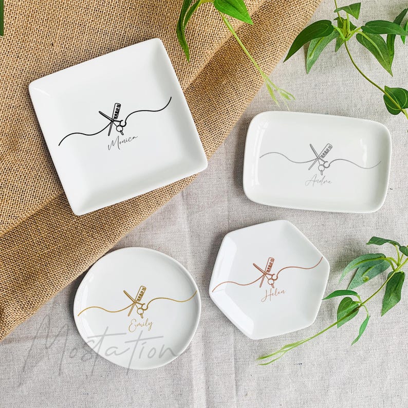 Pu&ograve; includere: Quattro piattini in ceramica bianca di forma quadrata, rettangolare, rotonda ed esagonale. Ogni piattino presenta un disegno al tratto di forbici e pettine con un nome stampato sotto: Monica, Andrea, Emily e Helen in vari colori.