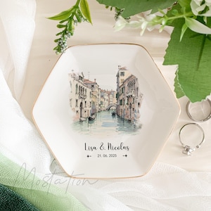 May include: White hexagonal ceramic ring dish with a gold rim. The dish features a watercolor illustration of a canal in Venice, Italy. The text "Lisa & Nicolas 21.06.2025" is printed on the dish.