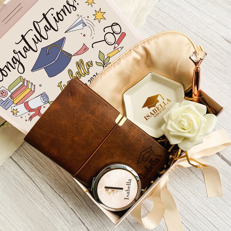Pu&ograve; includere: Una confezione regalo a tema laurea. Include un diario in pelle marrone, uno specchietto compatto, una mascherina per dormire, un piattino e una penna. La scatola contiene anche un fiore decorativo e una carta con il nome "Isabella".
