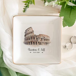 May include: White ceramic ring dish with a gold rim. The dish features a watercolor illustration of the Colosseum in Rome. The text "Christine & Jeff 06.07.2025" is printed below the illustration.