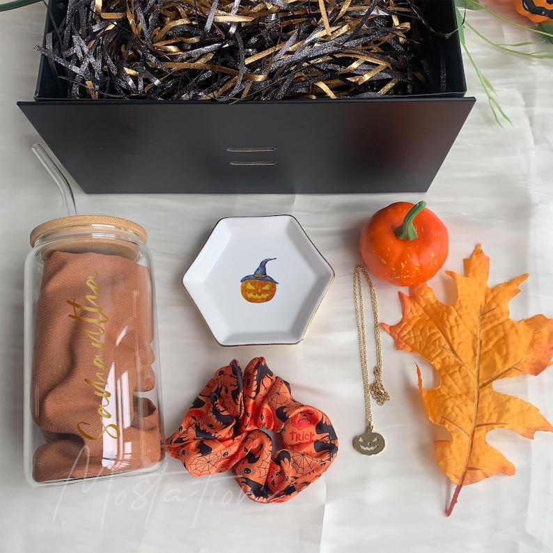 Pu&ograve; includere: Un set regalo composto da un bicchiere in vetro con coperchio in bamb&ugrave; e cannuccia, un piattino in ceramica esagonale bianco con illustrazione di zucca, un elastico per capelli arancione e nero, una collana con ciondolo a zucca dorato e una zucca finta.