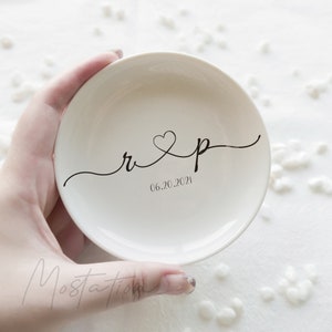 May include: A round, off-white ceramic trinket dish featuring black cursive lettering with the lowercase letters r and p connected by a heart symbol. Below the letters, the date 06.20.2021 is printed in a simple, clean black font.