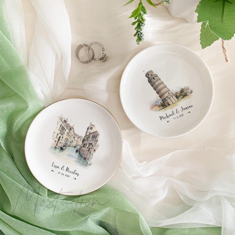May include: Two white ceramic ring dishes with gold trim. One dish features a watercolor illustration of the Leaning Tower of Pisa with the text "Michael & Janine 11.8.2020". The other dish features a watercolor illustration of a canal in Venice with the text "Lisa & Nicolas 21.06.2020".
