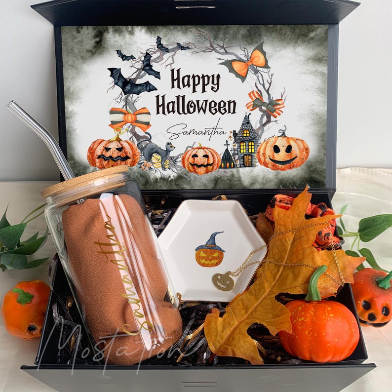 Pu&ograve; includere: Una scatola regalo nera contenente un bicchiere di vetro con coperchio in bamb&ugrave; e cannuccia in metallo, un panno marrone, un piattino esagonale bianco con illustrazione di zucca, una collana a zucca dorata e una foglia secca, con Happy Halloween.