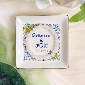 Op de afbeelding: Witte keramische schaal met een blauw-wit bloemenmotief en een citroenmotief. De schaal heeft de tekst "Rebacea & Matt 05.25.2025" en een witte kralenarmband.
