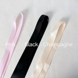 May include: Three lengths of smooth satin ribbon arranged vertically. The left ribbon is light pink, the center ribbon is black, and the right ribbon is champagne. The text Pink, Black, and Champagne is printed next to each corresponding ribbon.