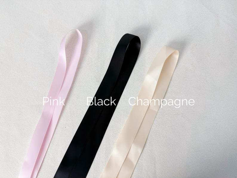 May include: Three lengths of smooth satin ribbon arranged vertically. The left ribbon is light pink, the center ribbon is black, and the right ribbon is champagne. The text Pink, Black, and Champagne is printed next to each corresponding ribbon.