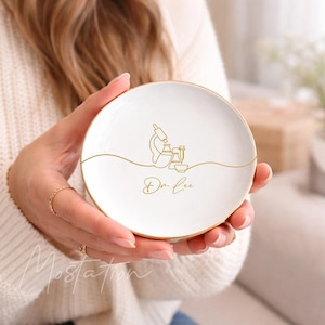 May include: White ceramic trinket dish with a gold rim and a gold line drawing of a microscope and lab equipment. The dish has the name "Dr. Lee" in gold script. A decorative item for a desk or vanity.