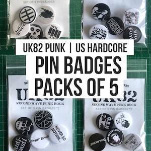 以下が含まれることがあります： 透明なプラスチック袋に入った、白黒のパンクロックピンバッジのセットが3つ。バッジには、「GBH」、「Never Ad Nothin...」、「The Exploited」、「Suicida Tendencia」、「Flag Black」、「Vice Squad」など、バンド名とロゴがデザインされています。