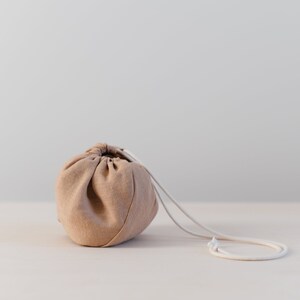 May include: A light brown drawstring bag with a white cord. The bag is sitting on a light wood surface.