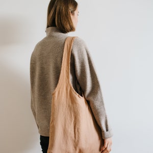 May include: A person wearing a gray sweater and black pants is carrying a large, light brown tote bag over their shoulder.