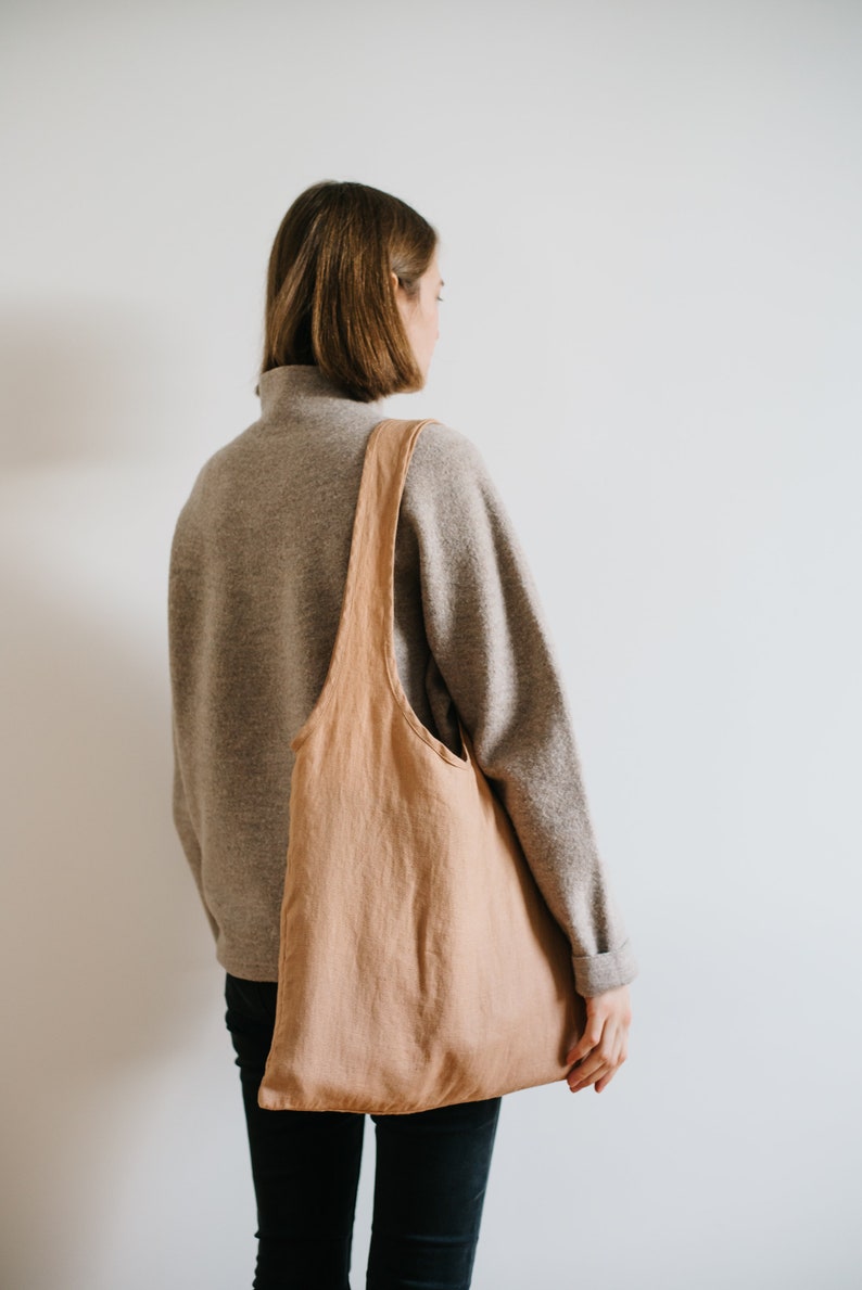May include: A person wearing a gray sweater and black pants is carrying a large, light brown tote bag over their shoulder.