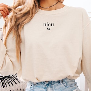 May include: A long-sleeved, ivory-colored sweatshirt with the text "nicu" and a small footprint graphic printed on the front.