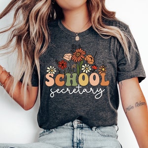 May include: Dark grey heather t-shirt with a floral design and the text "SCHOOL secretary" in colourful retro letters.