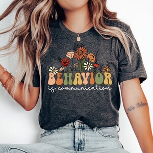 May include: Dark grey heather t-shirt with a floral design and the text "BEHAVIOR is communication".