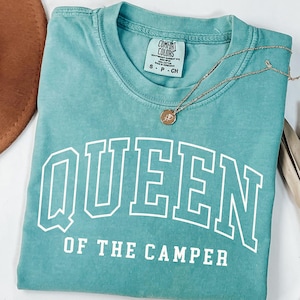 May include: Seafoam green t-shirt with the text "QUEEN OF THE CAMPER" in white. The shirt has a distressed look and is made of a soft, comfortable fabric.