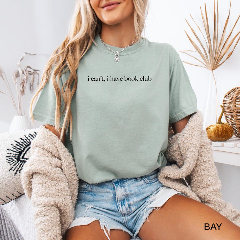 May include: A light green t-shirt with the text "i can't, i have book club" printed on the front.