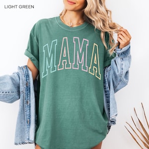 May include: A light green t-shirt with the word "MAMA" printed in rainbow colors. The shirt is oversized and has a relaxed fit.