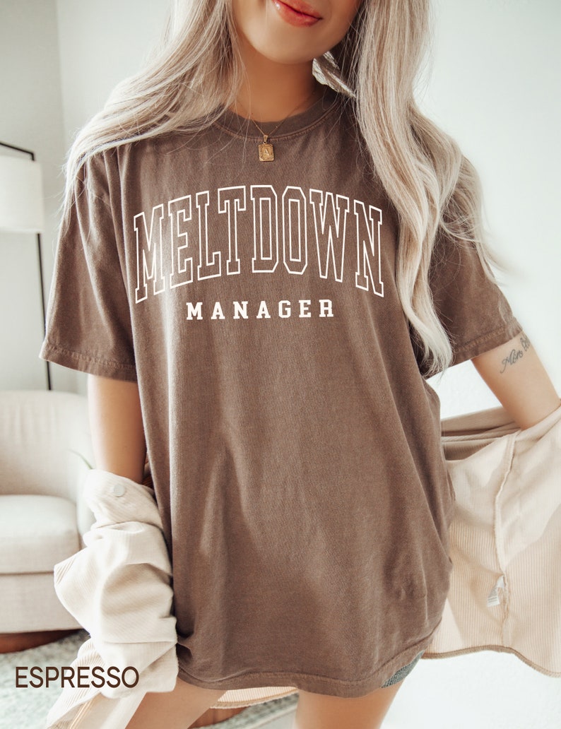 May include: A brown oversized t-shirt with the text "MELTDOWN MANAGER" printed in white.
