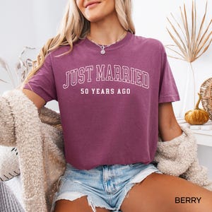 May include: Berry-colored t-shirt with the text "JUST MARRIED 50 YEARS AGO" in white block letters. The shirt is short-sleeved and has a relaxed fit. The word "BERRY" is printed in white at the bottom right corner of the image.