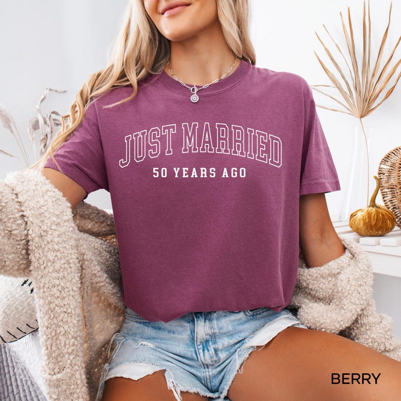 May include: Berry-colored t-shirt with the text "JUST MARRIED 50 YEARS AGO" in white block letters. The shirt is short-sleeved and has a relaxed fit. The word "BERRY" is printed in white at the bottom right corner of the image.