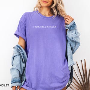 May include: A purple t-shirt with the text "i can't, i have book club" printed in white.