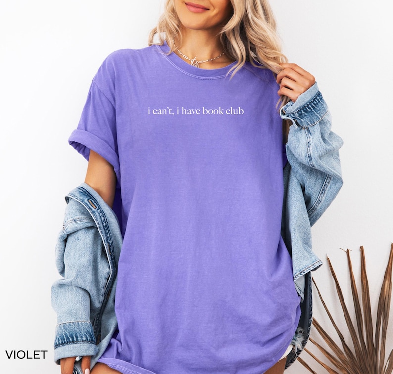 May include: A purple t-shirt with the text "i can't, i have book club" printed in white.