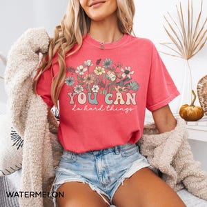 May include: A pink t-shirt with a floral design and the text "YOU CAN do hard things" in a retro font.