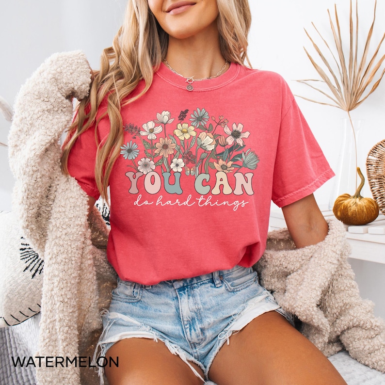 May include: A pink t-shirt with a floral design and the text "YOU CAN do hard things" in a retro font.