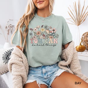 May include: A light green t-shirt with a floral design and the text "YOU CAN do hard things" in a retro font.