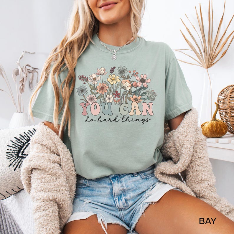 May include: A light green t-shirt with a floral design and the text "YOU CAN do hard things" in a retro font.