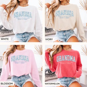 May include: White, ivory, blossom pink, and watermelon-colored sweatshirts. Each sweatshirt features the word "GRANDMA" in a light blue floral design, with the names "EMMA TYLER AVA HENRY JAMES" below.