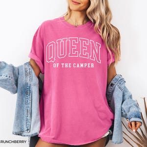 May include: A pink t-shirt with the text "Queen of the Camper" in white lettering. The shirt is a relaxed fit and has a crew neck.