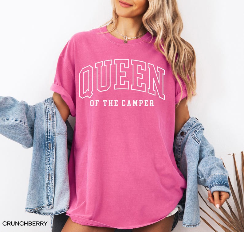 May include: A pink t-shirt with the text "Queen of the Camper" in white lettering. The shirt is a relaxed fit and has a crew neck.
