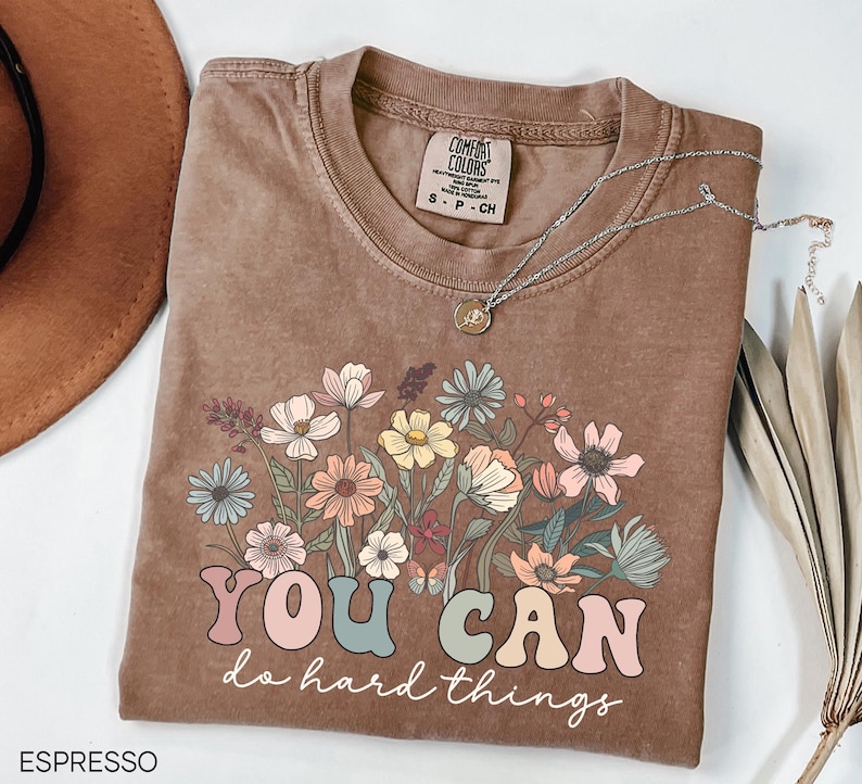 May include: A brown t-shirt with a floral design and the text "YOU CAN do hard things" in colorful letters.
