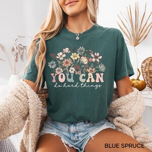 May include: A teal blue t-shirt with a floral design and the text "YOU CAN do hard things" in a colorful retro font.