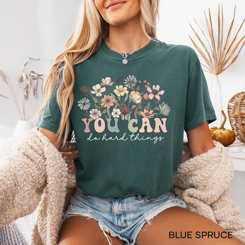 May include: A teal blue t-shirt with a floral design and the text "YOU CAN do hard things" in a colorful retro font.