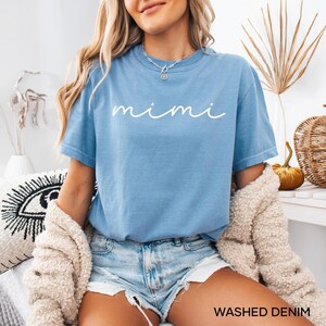 May include: A light blue t-shirt with the word "mimi" written in white cursive script. The shirt is made of a soft, comfortable material and has a relaxed fit.