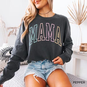 May include: A dark gray long-sleeved cropped sweatshirt with the word "MAMA" printed in rainbow colors across the front.
