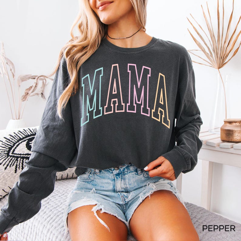 May include: A dark gray long-sleeved cropped sweatshirt with the word "MAMA" printed in rainbow colors across the front.