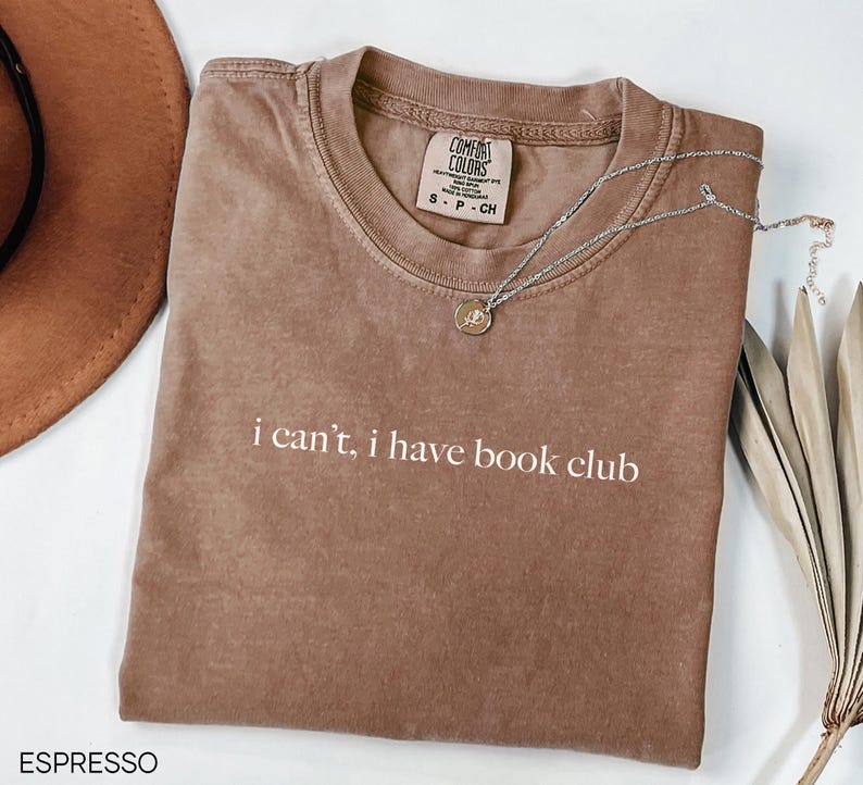May include: A brown t-shirt with the text "i can't, i have book club" printed in white. The shirt is made of a soft, comfortable material and has a relaxed fit.