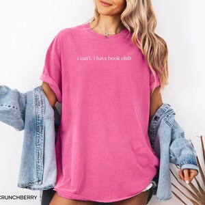 May include: A pink t-shirt with the text "i can't, i have book club" printed in white on the front.