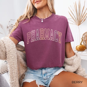 May include: A mauve t-shirt with the word "PHARMACY" printed in a rainbow arch design.